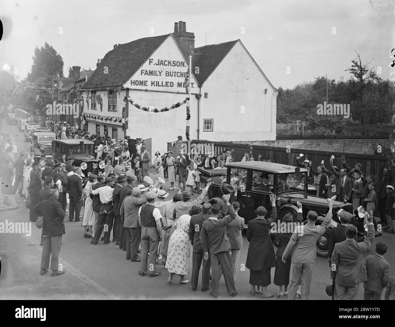 King et Queen font un détour de 3 kilomètres pour traverser un village en route vers Windsor. En réponse à une demande faite au Palais de Buckingham par les habitants de Colnbrook, un village sur la route de Bath le Roi et la Reine ont fait un détour de 2 miles sur leur route d'État de Londres à Windsor afin de passer par le village. La voiture royale a été ralentie à un rythme de marche et le capot a été abaissé de sorte que la foule puisse voir le roi et la reine et les princesses. Photos : la voiture royale a applaudi lorsqu'elle passait par le village de Colnbrooke. [La publicité murale se lit comme suit : F. Jackson Family Butchers, Home tué Meat Banque D'Images