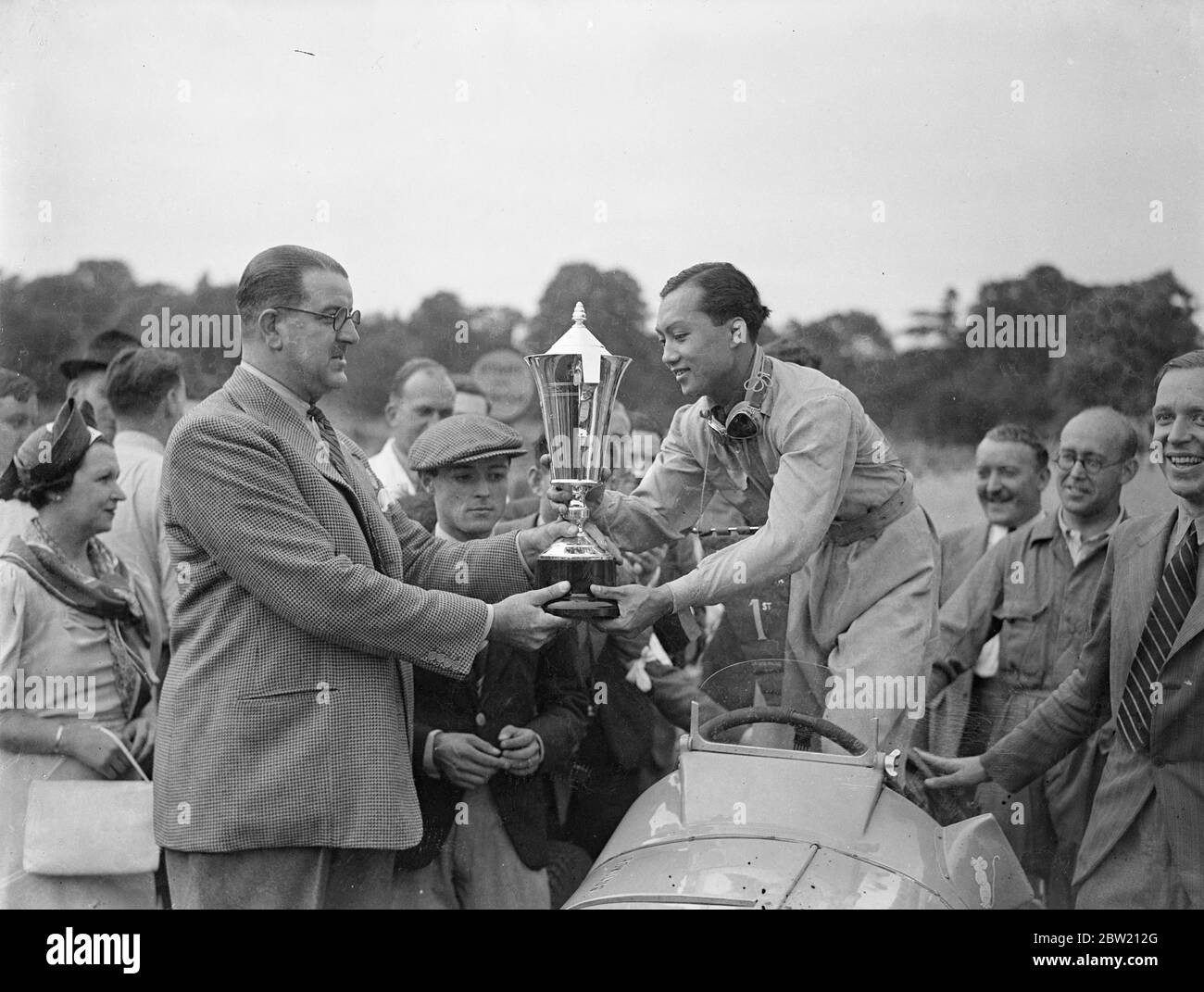Le Prince Birabongse de Siam [Prince Bira de Siam / Thaïlande], pilotant une ERA [automobiles anglaises] a remporté le premier Grand Prix de Londres sur le nouveau circuit de course de Crystal Palace. I. F. Cornell (ERA) est deuxième et P. Maclure (Riley) troisième. Le Prince Birabongse reçoit la coupe de M. Charles Follett. En tête est le prince Chula de Siam [prince Chula Chakrabongse de Siam]. 17 juillet 1937 Banque D'Images