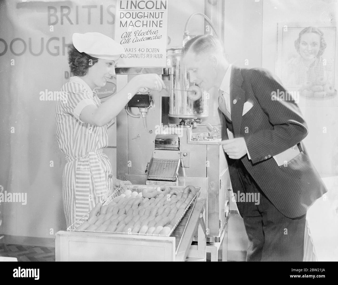Le visiteur goûte un donut de la machine à l'exposition des boulangers au Royal Agricultural Hall, Islington, Londres. Cette machine, qui fait des beignets d'une formule secrète a évolué après des années de recherche, s'est avéré 40 douzaines de pâtisseries en une heure. 6 septembre 1937. Banque D'Images