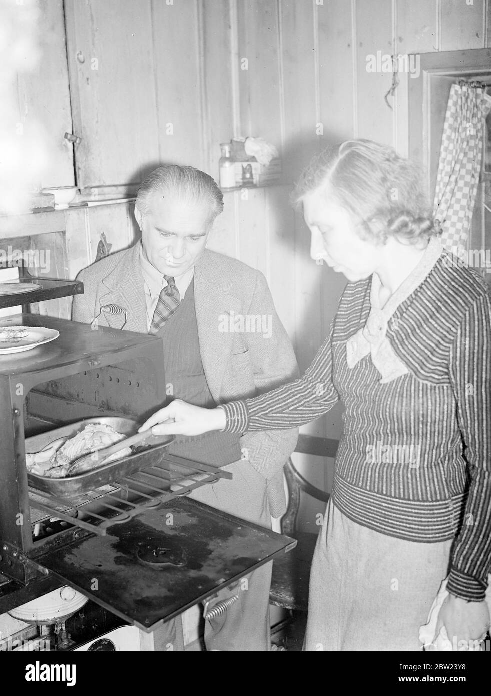 Du luxe d'un château de 60 pièces dans le Tyrol autrichien, le comte Lesven Zeppelin, neveu de 42 ans du concepteur de navires aériens allemand, et sa belle femme anglaise ont été forcés de chercher le sanctuaire d'un cottage de cinq pièces délabré dans le sud de Warnborough, près de Basingstoke, Hampshire. Le comte a perdu sa fortune après que Hitler ait annexé l'Autriche. La comtesse, qui a épousé le comte il y a neuf ans, fait maintenant sa propre cuisine. Le comte Lesvan Zeppelin a fait une exploration dans la jungle bolivienne il y a 14 ans. Spectacles photo: La comtesse cuisant le dimanche dîner sur un poêle à huile à leur chalet A. Banque D'Images