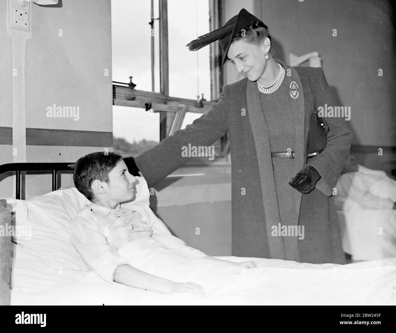 La duchesse de Kent a visité les quartiers avec patience après avoir posé la pierre de fondation d'une nouvelle aile de l'hôpital municipal de Southend à Rochford, dans l'Essex. Photos: La duchesse de Kent, la main reposant sur le lit, sourit alors qu'elle discute avec Dennis Collingwood, neuf ans, qui est traité pour appendicite. 12 octobre 1938 Banque D'Images