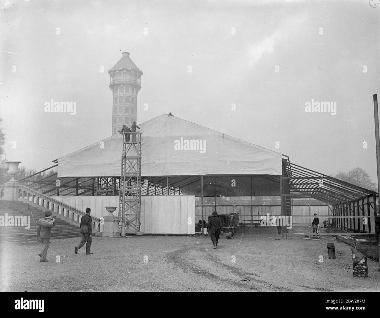 Crystal Palace est d'avoir une autre exposition. Alors que les ouvriers sont encore en train de retirer les ruines de l'ancien Crystal Palace, détruit par un incendie en 1936, d'autres ouvriers dressent des pavillons pour l'ouverture de l'exposition du sud de Londres sur le terrain en mars prochain. Des spectacles photo, l'un des pavillons de l'exposition du Sud de Londres, qui s'élève sous la tour de l'ancien Palais de Cristal. 8 janvier 1938 Banque D'Images