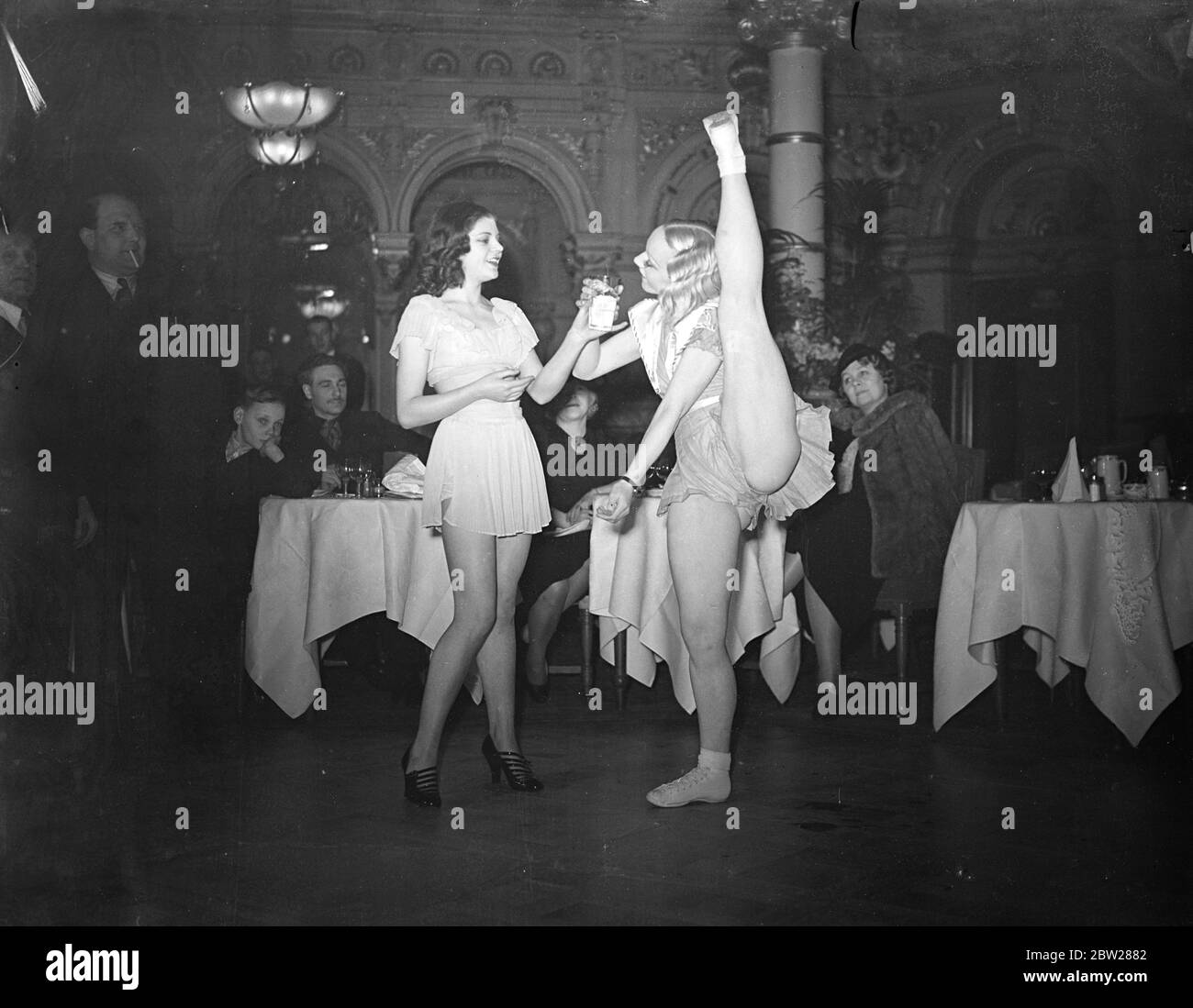 Rafraîchissement pour fille essayant le record mondial de coup de pied à Londres. Mlle Veronica, titulaire du record mondial de coups de pied, a tenté de battre son propre record lors du championnat du monde au restaurant Frascati's, à Oxford Street. Elle a dû faire plus de 3000 coups de pied consécutifs. La photo montre que Mlle Veronica se rafraîchit pendant sa tentative de record. Elle devait continuer à donner des coups de pied pendant qu'elle l'a bu. 6 janvier 1938 Banque D'Images