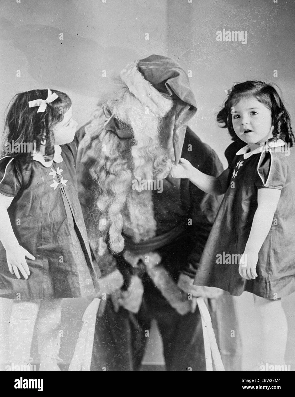 Les Quins ont passé un joyeux Noël, a découvert 'Santa' Dafoe. Bien que strictement confinées à leur pépinière Callender (Ontario), les quintuplets de Dionne ont passé un très joyeux Noël. Le moment le plus joyeux du jour, en dehors de déballer leurs nombreux cadeaux, a été la découverte du Dr Dafoe se faisant passer pour le Père Noël. Astute Yvonne et Annette ont démasqué le médecin. Des spectacles de photos, Yvonne et Annette Peer inquemment au Père Noël, qu'ils commencent à soupçonner est leur propre Dr Dafoe. 2 janvier 1938 Banque D'Images