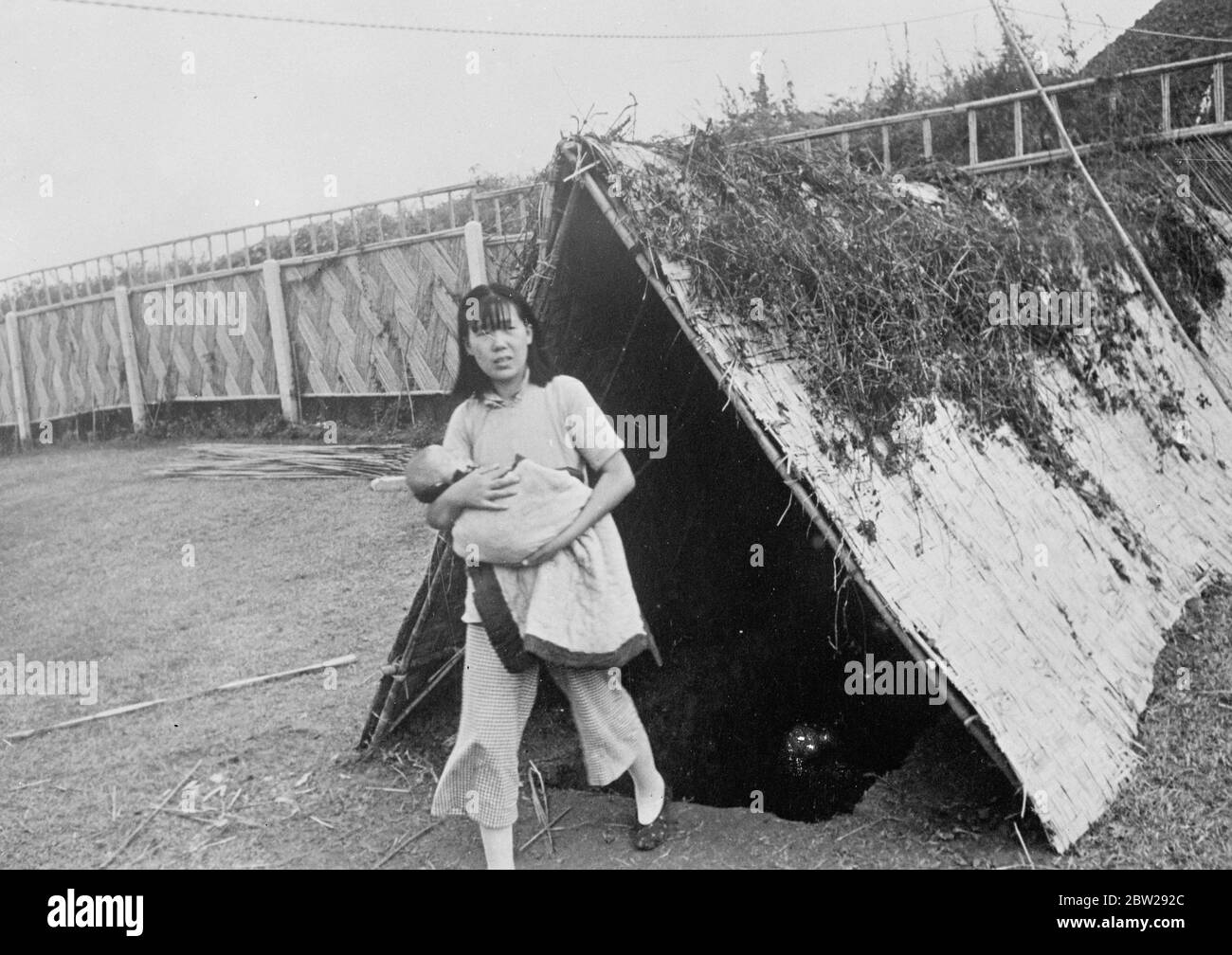 Les femmes et les enfants vont sur Terre à Shanghai. Dugouts camouflage contre les attaques aériennes. Les dugouts, dont l'entrée est dissimulée par des tentes camouflage avec du feuillage pour les rendre invisibles aux raiders aériens japonais, fournissant un abri sûr aux femmes et aux enfants dans Shanghai ravagé par la guerre. Photos, la jeune fille chinoise, groupage, un petit bébé dans ses bras, émergeant d'un camouflage dugout à Shanghai. 31 octobre 1937 Banque D'Images