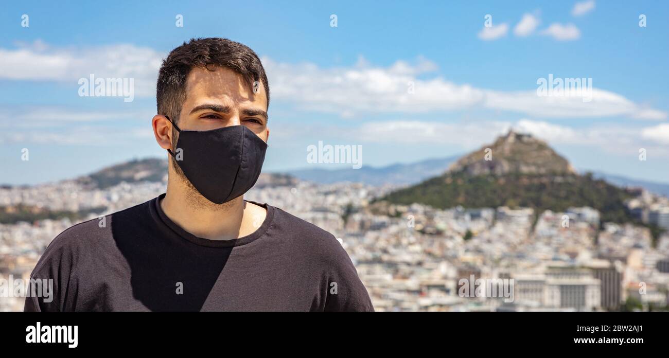 Athènes Grèce coronavirus Days. Jeune homme portant un masque de protection, paysage urbain d'Athènes avec support Lycabette et fond bleu ciel. Banque D'Images