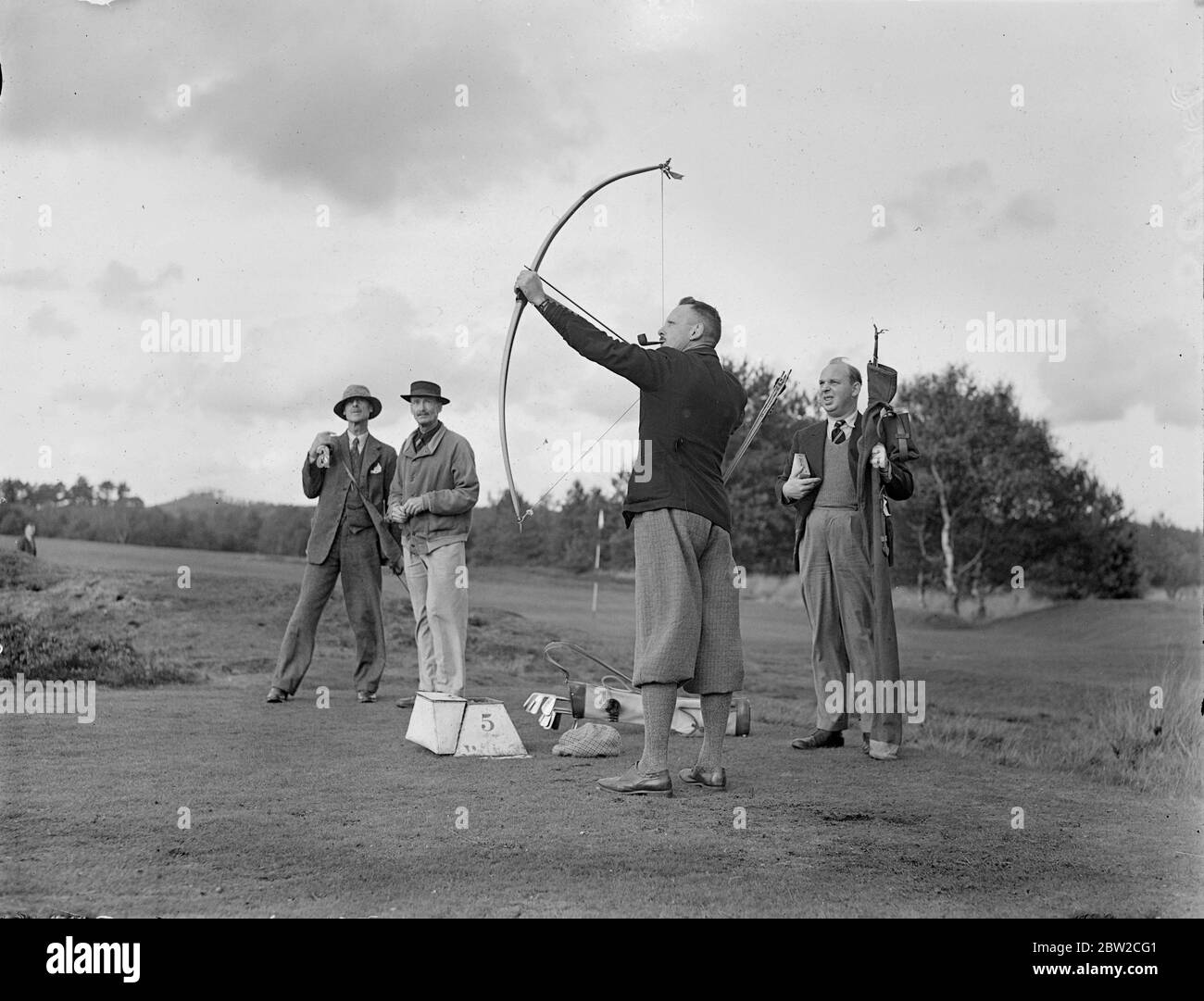 Jouant avec Bow et Arrow, le major J G Hayter, expert reconnu dans le sport annuel du golf Bow et Arrow, a rencontré le colonel E St George Kirke, le capitaine du club, dans un match au Hankley Common Golf Club, Surrey. Il a concédé un coup un gale.le major Hayter tire sa flèche dans une boîte au lieu d'un trou.sa moyenne pour la plupart des cours de Surrey est dans les années 70. Photos : le Major J G Hayter photographie une flèche. 18 octobre 1938 Banque D'Images