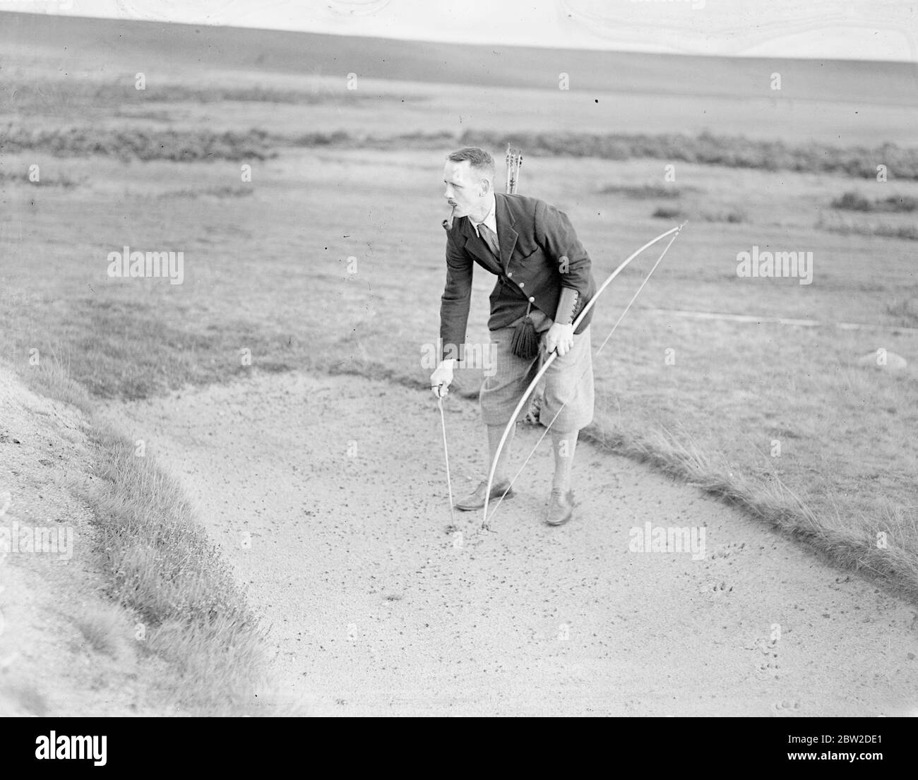 Jouant avec Bow et Arrow, le major J G Hayter, expert reconnu dans le sport annuel du golf Bow et Arrow, a rencontré le colonel E St George Kirke, le capitaine du club, dans un match au Hankley Common Golf Club, Surrey. Il a concédé un coup un gale. Le major Hayter tire sa flèche dans une boîte au lieu d'un trou. Sa moyenne pour la plupart des cours de Surrey est dans les années 70. Photos montre: Le major J G Hayter piller sa flèche d'un bunker, perdant ainsi un coup ou un coup de feu. 18 octobre 1938 Banque D'Images