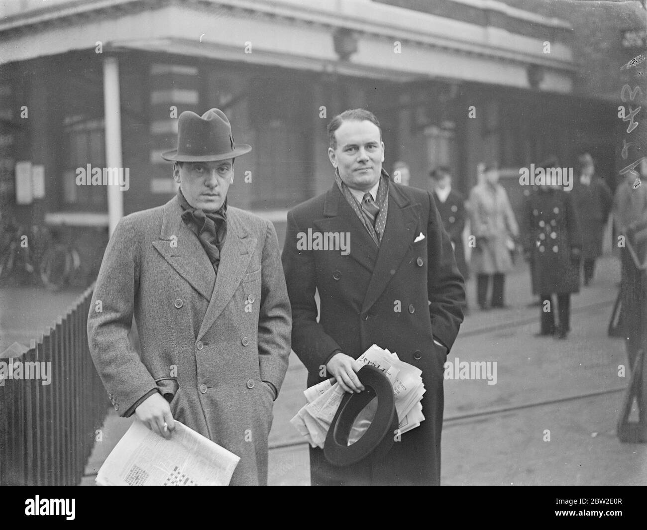 Deux hommes non sous-titrés tenant des journaux à l'extérieur d'une gare ferroviaire Banque D'Images