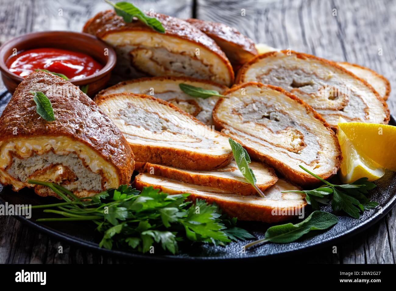 Gros plan du fromage omelette rouler avec garniture de viande hachée sur une assiette noire avec citron, ketchup et persil sur une table en bois gris, vue sur le paysage Banque D'Images