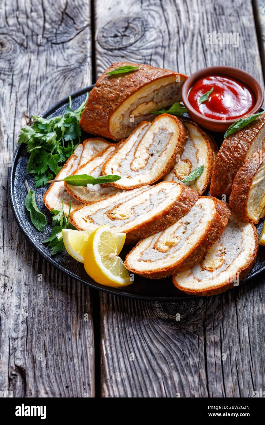 Au four omelette au four rouler avec garniture de viande hachée sur une assiette noire avec citron, ketchup et persil sur une table en bois gris avec fourchette dorée et k Banque D'Images