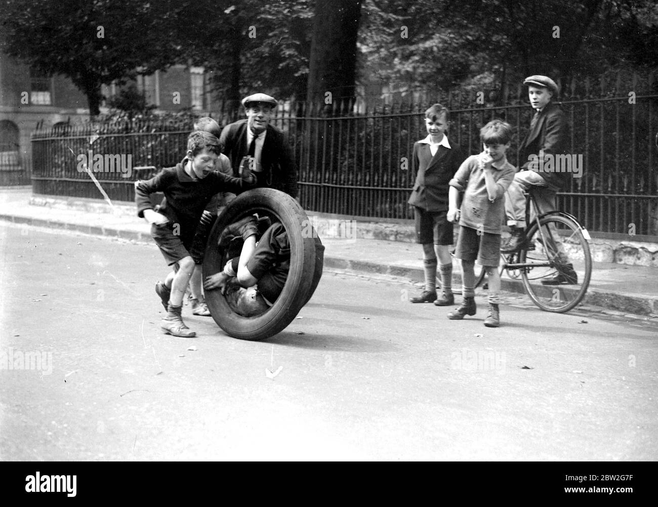 Les enfants jouent avec un vieux pneu surveillé par d'autres garçons. 1934 Banque D'Images