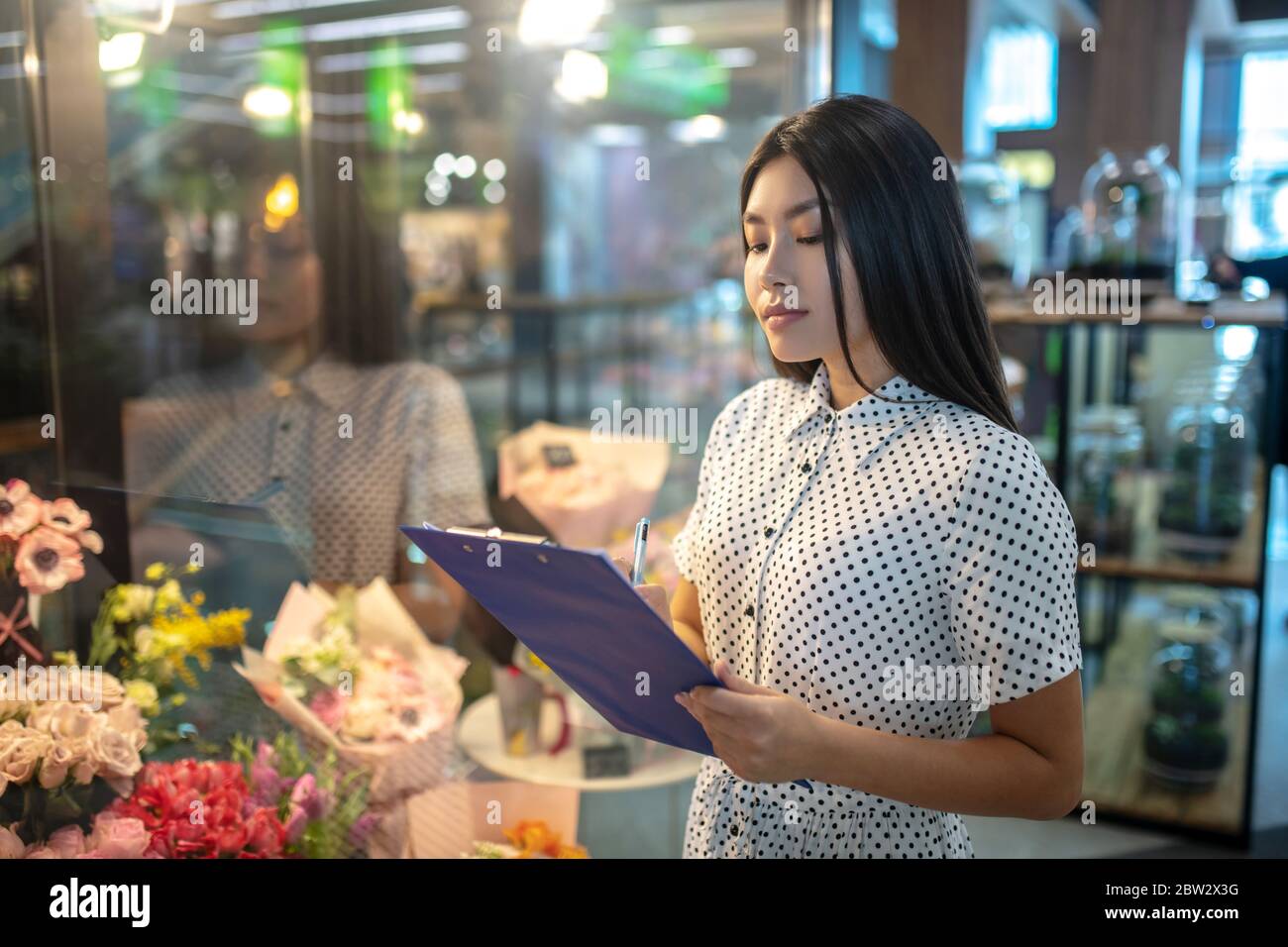 Brunette femme debout devant des fleurs, prenant des notes Banque D'Images