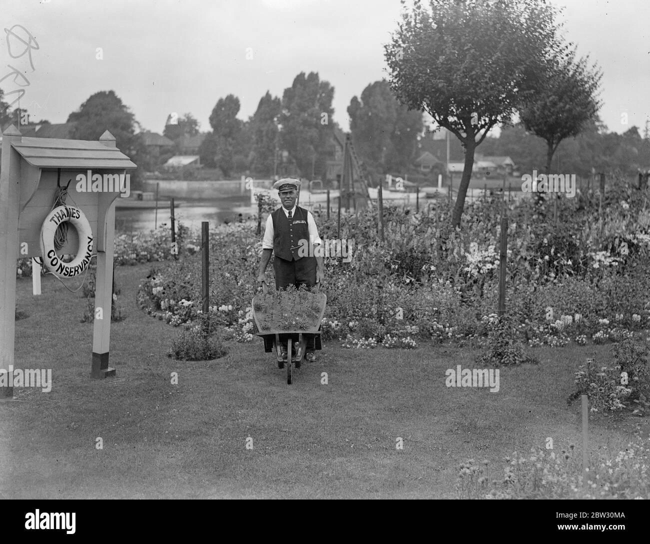 Le gardien de serrure de Teddington remporte la coupe de défi Sir Reginald Hanson pour les jardins de serrures les mieux gardés pour la troisième fois . Pour la troisième fois , M. A E Allen , gardien de l'écluse de Teddington , sur la Tamise, a reçu la coupe Sir Reginald Hanson Challenge pour les jardins les mieux gardés de l'écluse le long de la tamise . M. A E Allen ( à gauche ) marchant dans les jardins avec un de ses assistants . 27 juillet 1932 Banque D'Images