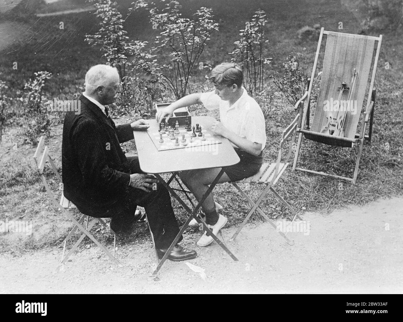 Célèbre violoniste de garçon , Yehudi Menuhin , en vacances . Yehudi Menuhin , violoniste de 15 ans qui a déjà gagné la renommée mondiale , passe des vacances près de Paris avant de venir à Londres pour une saison . Il fera une tournée en Amérique plus tard dans l'année . Yehudi Menuhin jouant aux échecs avec un vieil ami dans le jardin de sa maison de vacances près de Paris . 22 septembre 1932 Banque D'Images