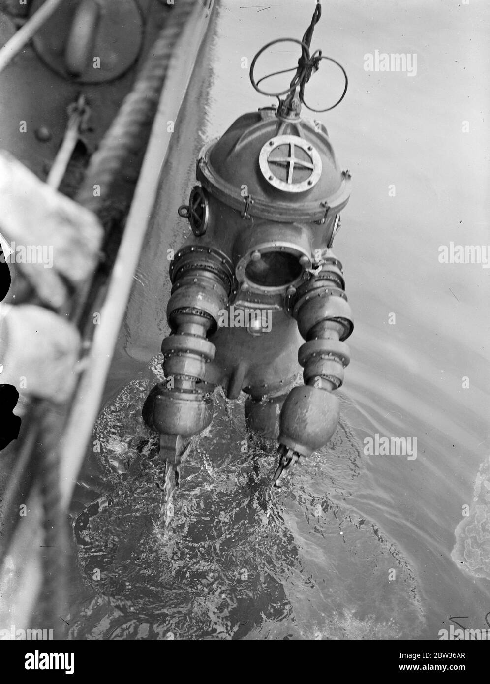 Nouvelle robe de plongée subit des tests en haute mer . Une robe de plongée inventée par M. J S Peress de Byfleet , Surrey , a subi des tests de performance en eau profonde en mer au large de Portsmouth . Il a été pris dans HMS Tedworth . La robe est un cylindre en acier avec un sommet en forme de dôme , qui est la tête , à laquelle sont attachés des pieds et des bras flexibles . Les bras sont fournis avec des pinces - comme des griffes comme des mains. La robe permet de plonger à des profondeurs beaucoup plus grandes que celles qui sont actuellement possibles . Un plongeur portant le nouvel appareil entrant dans l'eau du HMS Tedworth pour l'essai . 17 juin 1933 Banque D'Images