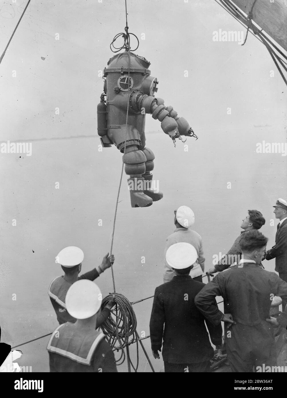 Nouvelle robe de plongée subit des tests en haute mer . Une robe de plongée inventée par M. J S Peress de Byfleet , Surrey , a subi des tests de performance en eau profonde en mer au large de Portsmouth . Il a été pris dans HMS Tedworth . La robe est un cylindre en acier avec un sommet en forme de dôme , qui est la tête , à laquelle sont attachés des pieds et des bras flexibles . Les bras sont fournis avec des pinces - comme des griffes comme des mains. La robe permet de plonger à des profondeurs beaucoup plus grandes que celles qui sont actuellement possibles . Un plongeur portant le nouvel appareil étant soulevé dans l'eau du HMS Tedworth pour l'essai . 17 juin 1 Banque D'Images