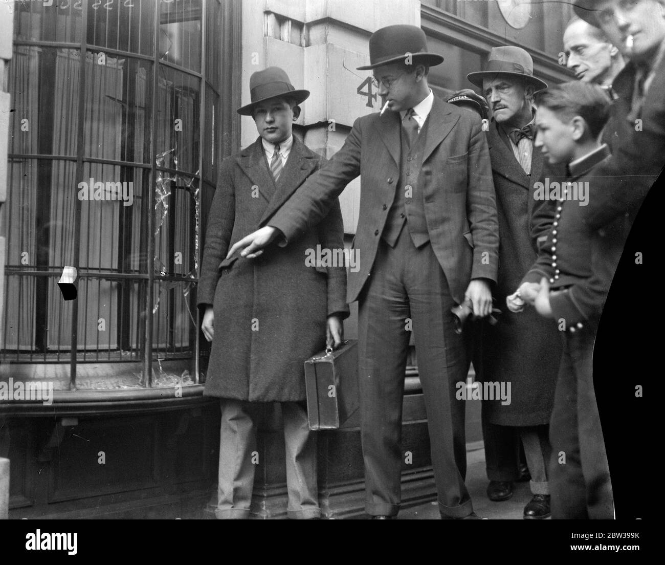 Bijoux d'une valeur de 7,000 £ volés dans le West End raid , trois hommes dans une voiture . Trois hommes dans une voiture ont conduit jusqu'aux locaux de Messrs . J R Ogdens , judéliers de cour , rue Duke . Un des hommes est sorti et a cassé le verre de la plaque avec un instrument de fer . Il a attrapé des bijoux à la valeur de £7, 000 , est retourné à la voiture et a conduit . L'alarme a été donnée par Reginald Knife un messager, mais les raids ont disparu . Photos ; le directeur de la bijouterie , MR R Avison , avec Reginald Knife le messager après le raid . Le gestionnaire pointe vers le trou fait par les bandits . 17 F Banque D'Images