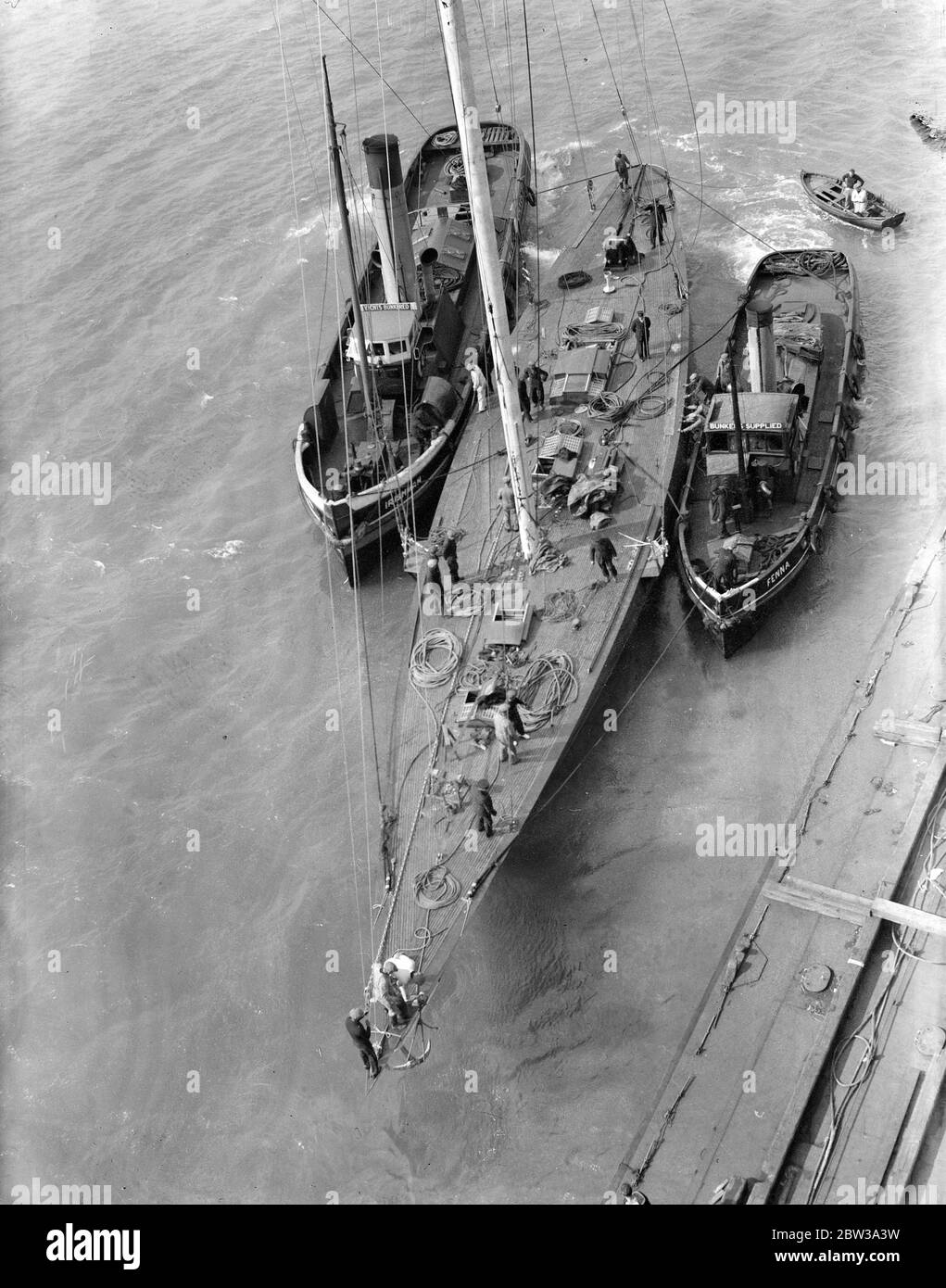 L ' espoir de yachting de Grande-Bretagne a son mât mis en place par grue géante . M. T O M Sopowy ' s America ' s Cup challenger a été remorqué à Portsmouth Dockyard pour faire marcher son mât ' ou mis en place . Le mât géant , qui est , comme la coque , en acier , est de 167 pieds de haut , presque la même colonne que Nelson ' s dans Trafalgar Square , Londres . Photos montre , regardant vers le bas sur le pont de l'Endeavour , l'espoir de la Grande-Bretagne qui hurlait comme son mât a été placé en position . Cette photo a été prise du sommet de la grue géante . 20 avril 1934 . Banque D'Images