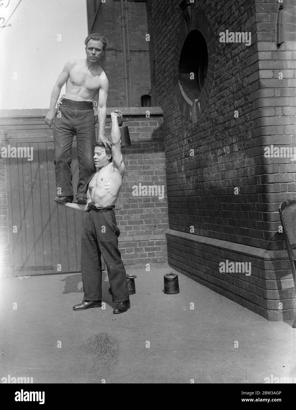 Cirque acrobat hommes forts pratiquant une routine dans une cour en brique . Un homme se tient équilibré sur l'avant-bras d'un autre Banque D'Images