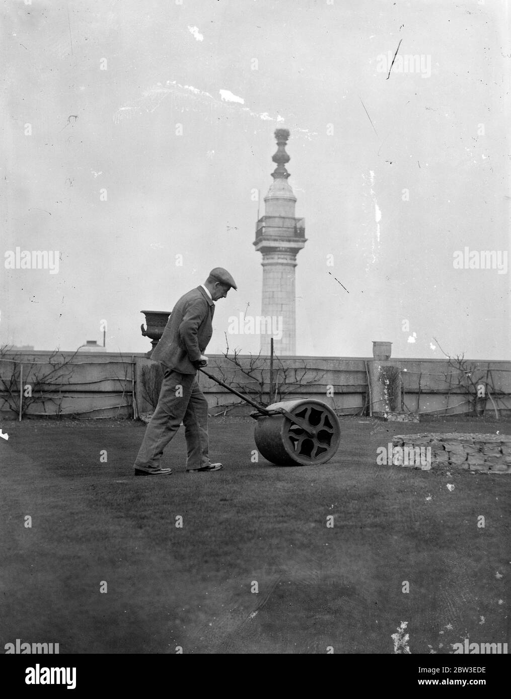 Roulant sur un toit de Londres vert d'exercice . Un rouleau vert est utilisé sur le toit d'un grand bâtiment de ville. Sur le toit est un vert d'entraînement de seize trous qui est favorisé par les travailleurs de bureau par temps chaud . 5 février 1935 Banque D'Images