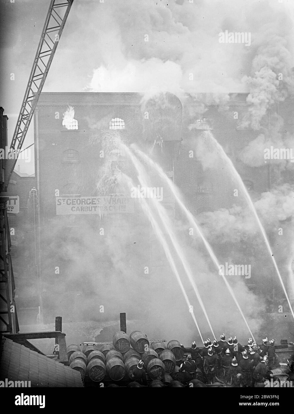 250 pompiers combattent le feu de l'entrepôt de riz de londres. Les moteurs de chacune des 60 stations de la LCC ont été appelés à un incendie énorme à St Georges ' s Wharf , un entrepôt de riz de Carbutt and Company , Ltd . à Shad thames , Bermondsey , Un appel d'urgence a été effectué et tous les appareils disponibles ont été envoyés . Environ 250 hommes ont été concentrés sur l'épidémie . Les pompiers portaient des masques à gaz contre la fumée dense du riz , et une tour d'eau géante de plateau tournant a été introduite dans l'opération . On craignait qu'un mur ne s'écroule . Photos montre , eau des tuyaux de tuyau en cascade sur le bâtiment en feu . Banque D'Images