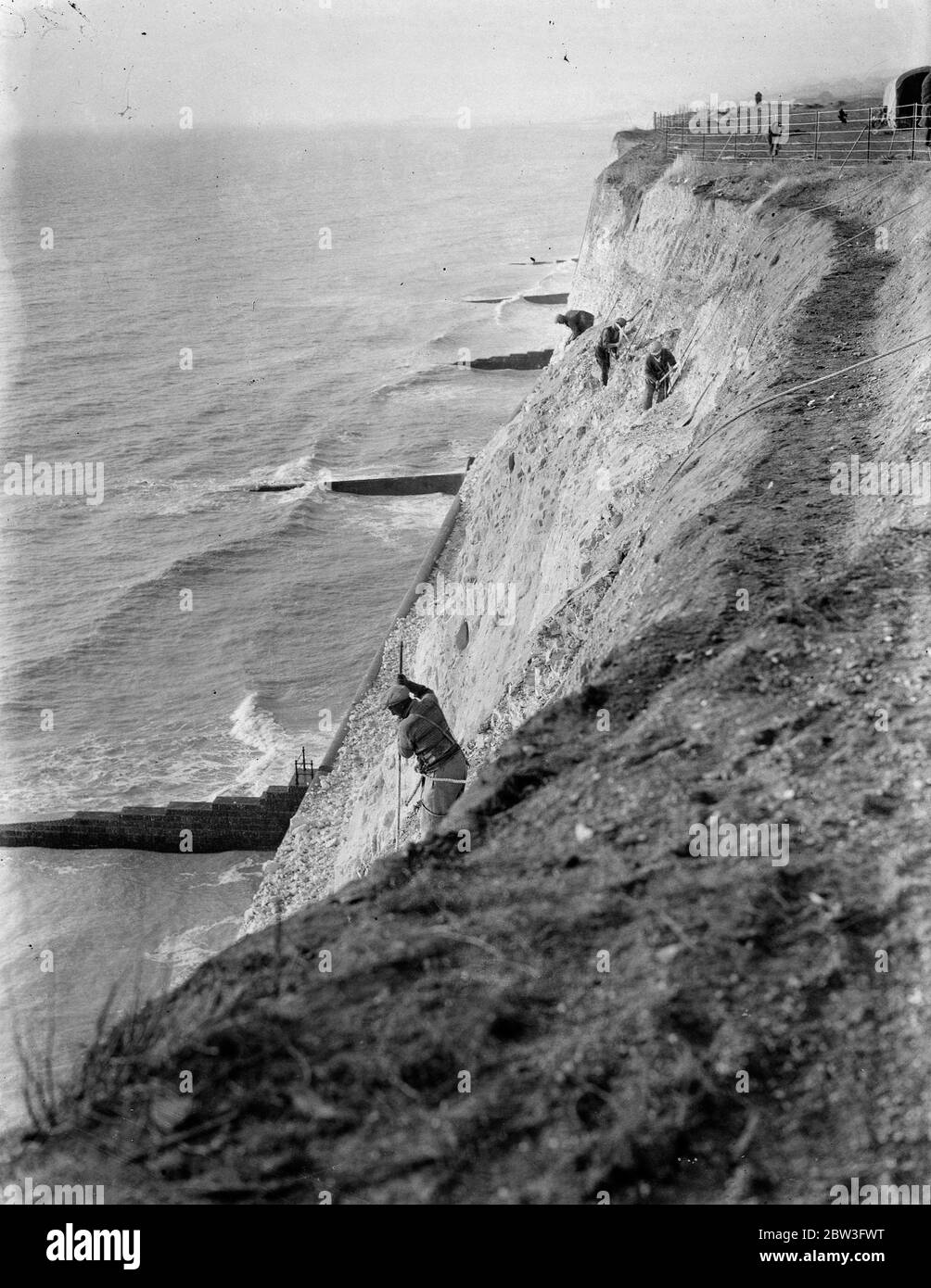 Des gradateurs de falaises attachés à des cordes au travail, au-dessus des vagues à Rotingdean, défaisant de dangereuses roches surplombant la promenade en bord de mer. 6 février 1935 Banque D'Images