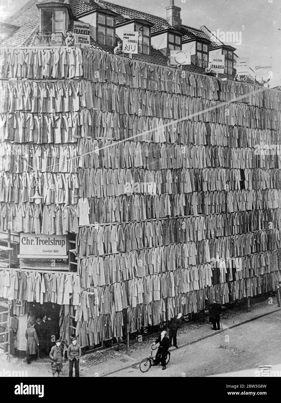 Boutique à l'intérieur du stock ! . La construction cachée par mille pardessus , apporte le chaos , mais tous ont été vendus . Tous les records en matière de vente à grande vitesse ont été brisés par M. Christiian Troelstrup , un habilleur de Copenhague qui voulait se débarrasser d'un grand stock de manteaux , M. Troelstrp a drapé ses manteaux , plus d'un millier d'entre eux , dans tout son bâtiment . Les murs de toiture à chaussée sont devenus une vaste étendue de revêtement , et bientôt les clients sont venus . Des centaines d'entre eux . Il fallait appeler la police supplémentaire pour s'occuper de la foule qui est venue la première à regarder puis à acheter . Au moment où les policiers harcelés ha Banque D'Images