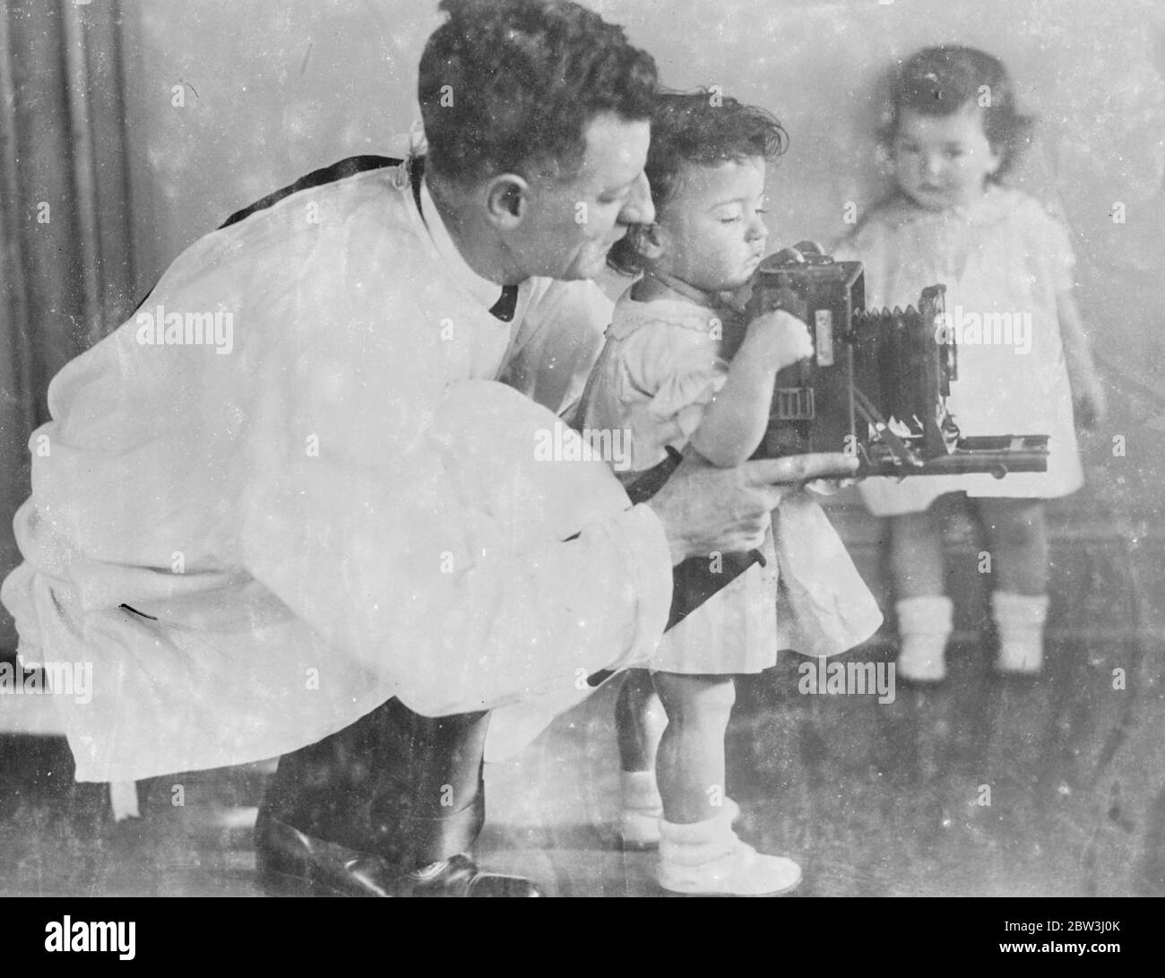Les Quins apprennent comment il a fait . Les Quintuplets de Dionne , la plupart des bébés photographiés dans le monde , sont parfois imprégnés du désir de tout savoir sur l'instrument intéressant dans les mains du caméraman . Leur bébé comme la curiosité a souvent des résultats désastreux pour l'appareil photo ! . Expositions de photos , Emilie reçoit quelques instructions de dernière minute de Fred Davis , le photographe de Quins, comme Annette pose contre le mur de la pépinière à Callender , en Ontario . Comme chaque visiteur la pépinière Quins , Dvis doit porter un manteau blanc . 12 juillet 1936 Banque D'Images