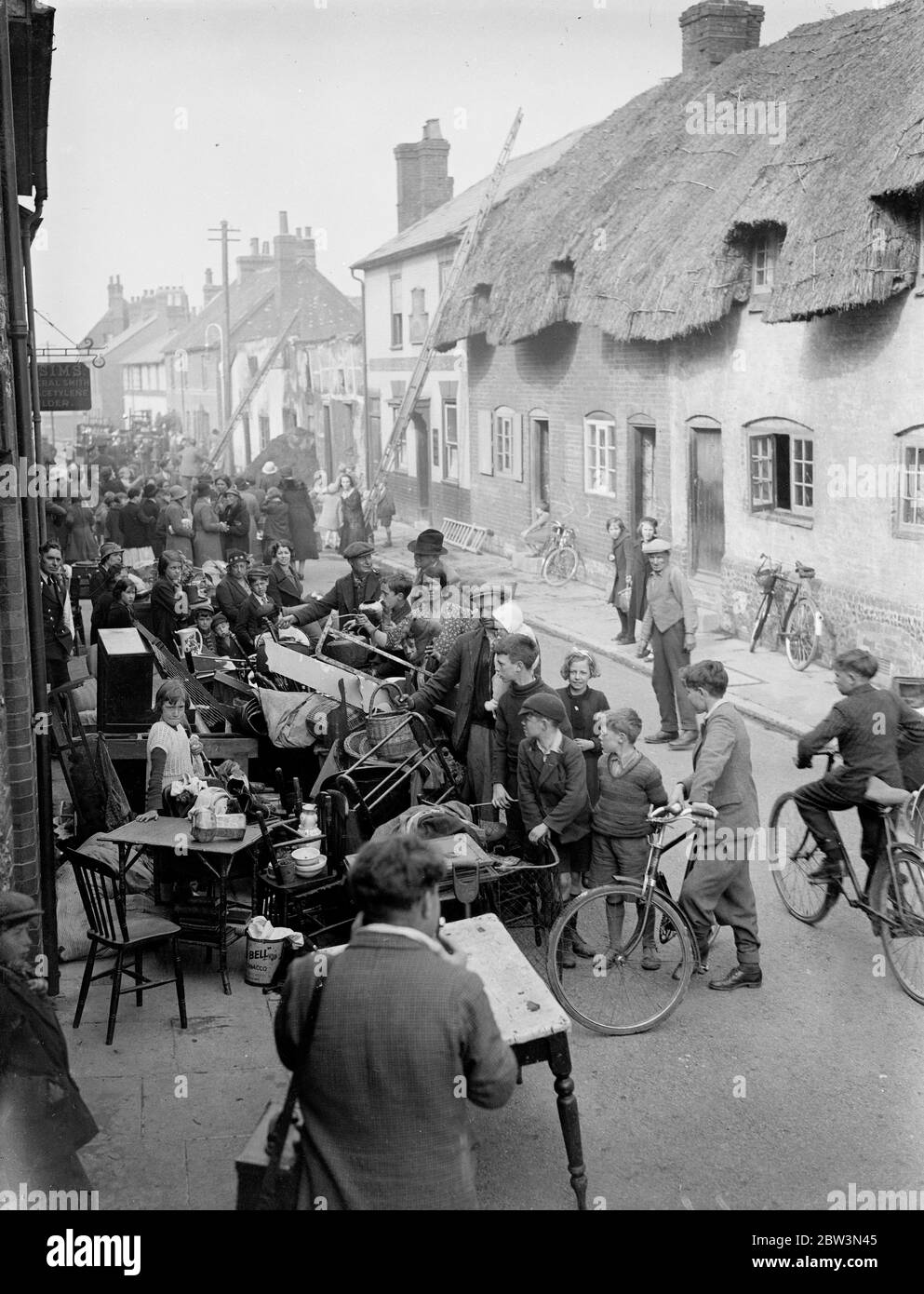 Quatre cottages de chaume ablasement dans le grand feu à Andover . Quatre maisons de Twatches ont fait fureur dans l'un des pires incendies vus à Andover ( Hampshire ) pendant 35 ans . Tandis que des dizaines d'aides essayaient de sauver les meubles des cottages condamnés , des pompiers ont cherché à empêcher les flammes de se propager à de nombreux autres cottages en chaume à proximité . Dix-huit personnes sont sans abri à cause du feu , m. et mme Bacon , une des familles qui ont perdu leur maison, ont six enfants . Photos spectacles , meubles empilés dans la rue après le feu . les cottages brûlés peuvent être vus en arrière-plan . 8 mai 1936 Banque D'Images