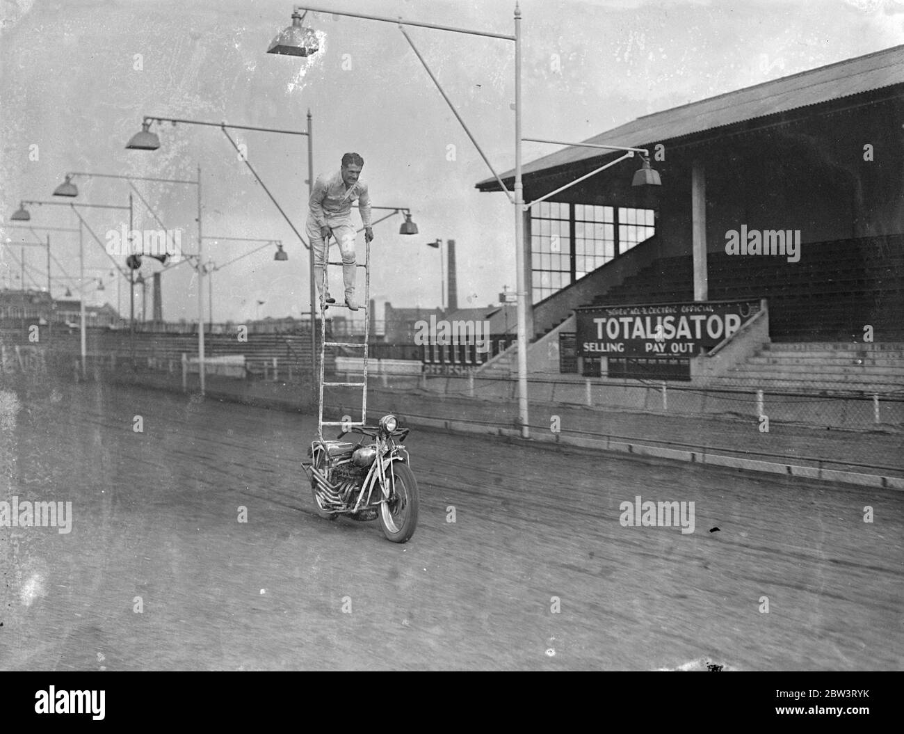 Il ' s au-dessus du cyclisme de moteur ordinaire ! Une exposition à couper le souffle de l'acrobatique à vélo a été donnée au Hackney Wick Stadium , Londres , par Putt Mossman et des membres de son équipe de pilotes de course . Pour aider Mossman dans ses cascades, il y a son épouse , Mme Helen Mossman , et sa sœur , Mlle Dessie Grant . Mossman est la première équipe de course américaine à visiter l'Angleterre et ils doivent avoir des rencontres avec des équipes britanniques . Photos , Putt Mossman donne une démonstration de la commande ' à distance ' ! . 25 mai 1936 Banque D'Images