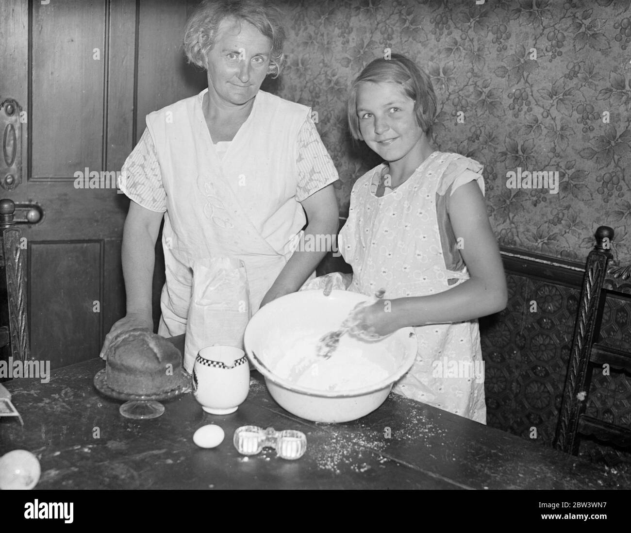 Mère apprend hpw ! . Fille de 10 ans gagne à la fabrication de gâteaux . Marjorie Tompsett, âgée de dix ans, d'Addiscombe , Surrey , a battu sa mère à la fabrication de gâteaux . Marjorie a réalisé son ambition lorsqu'elle a remporté le premier prix du concours de fabrication de gâteaux au salon annuel du Southern Railway à Croydon . Sa mère , qui entra aussi dans un gâteau de la même classe , était très commandée . Photos , Marjorie Tompsett faisant un gâteau regardé par sa mère . 20 août 1936 . Banque D'Images
