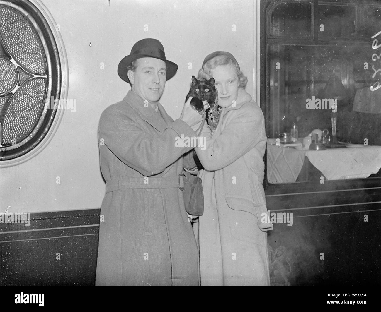 Les nibs vont à Hollywood . Charles Bennett prend la mascotte noire de chat . Nibs , un chat errant qui a erré dans leur appartement de Londres et a été adopté ' pour la chance ' , accompagné Charles Bennett , auteur des ' 39 étapes ' et ' sabotage ' , Et son épouse , Faith Bennett , quand ils ont quitté la gare de Waterloo sur le train de bateaux Normandie pour l'Amérique . M. Bennett a obtenu un contrat de cinq ans à Hollywood . Photos , M. et Mme Charles Baennet avec leur mascotte noire cas , leurs nibes , au départ de Waterloo . 11 mars 1937 Banque D'Images