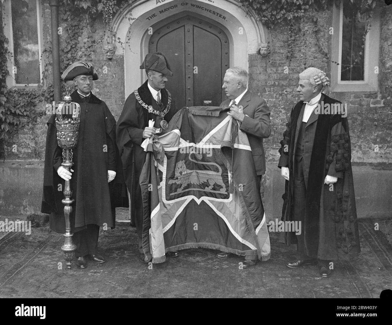 Le maire de Winchester (Virginie) présente le drapeau au maire de Winchester (Angleterre). Le maire de Winchester, Virginie, États-Unis, a présenté au maire de Winchester, Hampshire, au Winchester Guildhall, le grand drapeau de soie, la clé et le scrawl inscrits qui sont le cadeau de l'American Winchester aux habitants de leur ville de nom anglais. Le drapeau est une réplique du drapeau de la ville de Winchester, Virginie. Photos : le maire de Winchester, en Angleterre, le conseiller A. T. Edmonds (robes) et le maire de Winchester (Virginie), le Dr C. R. Anderson, avec le drapeau. Le greffier de la ville, M., se trouve à droite Banque D'Images