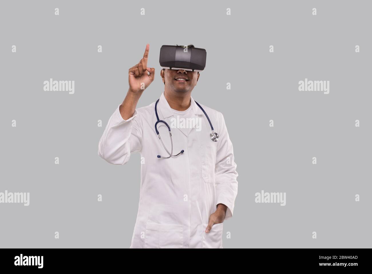Médecin portant des lunettes VR tapotant isolé. Indian Man Doctor pointant dans la réalité virtuelle Banque D'Images