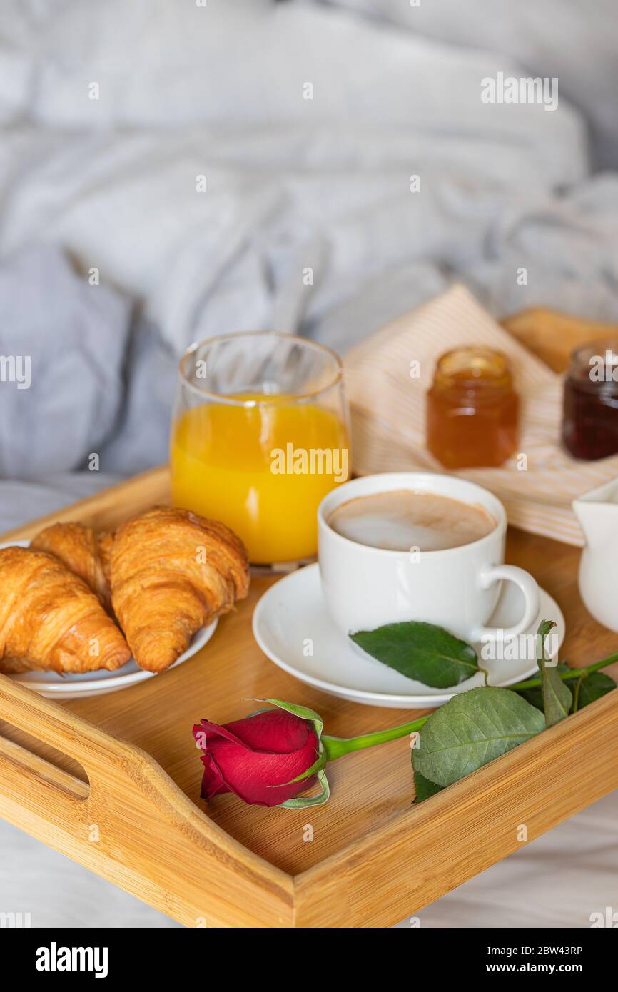 Petit déjeuner sur le lit dans une chambre. Essayez en bois avec du café,  du jus d'orange, un croissant avec de la confiture et une fleur de rose  rouge. Surprise romantique Photo