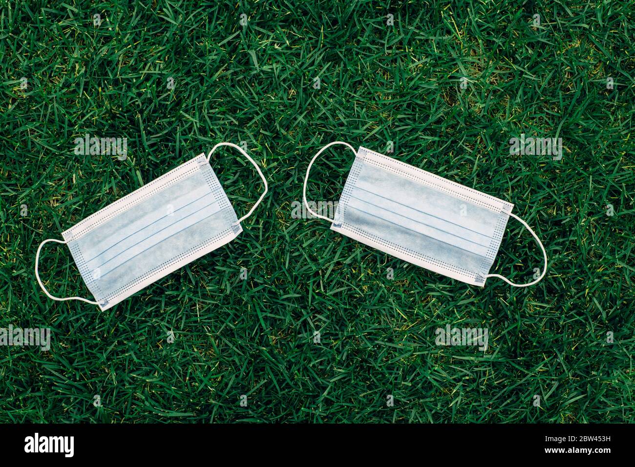 Deux nouveaux masques sanitaires frais posés sur le sol de l'herbe. Masque jetable recyclable plat. Coronavirus, médecine et allergie saisonnière concept. Vue Banque D'Images