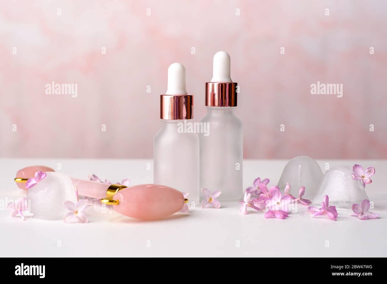 Bouteilles cosmétiques d'huile essentielle, rouleau de massage du visage et fleurs de lilas sur fond rose. Aromathérapie, concept de soin du visage. Banque D'Images