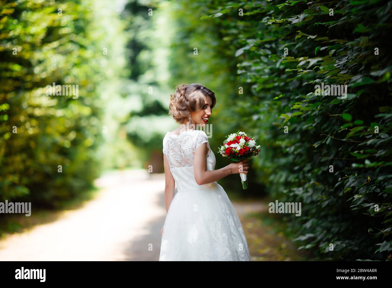 brunette mariée dans une robe avec un bouquet de mariage dans le parc sur un fond de verdure. Banque D'Images