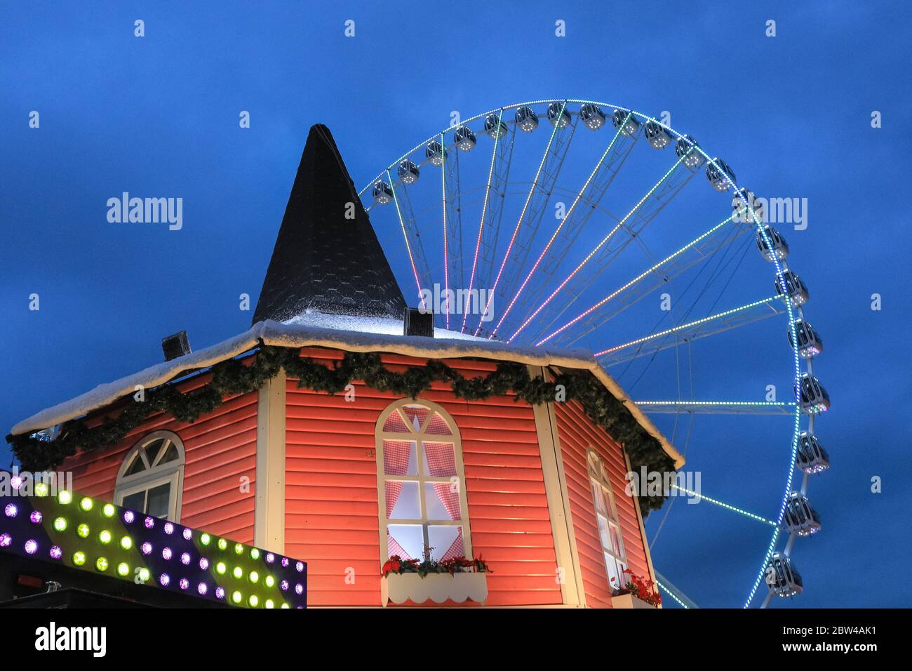 Grande roue illuminée la nuit, avec un stand de parc d'expositions, Winter Wonderland Hyde Park, Londres, Royaume-Uni Banque D'Images