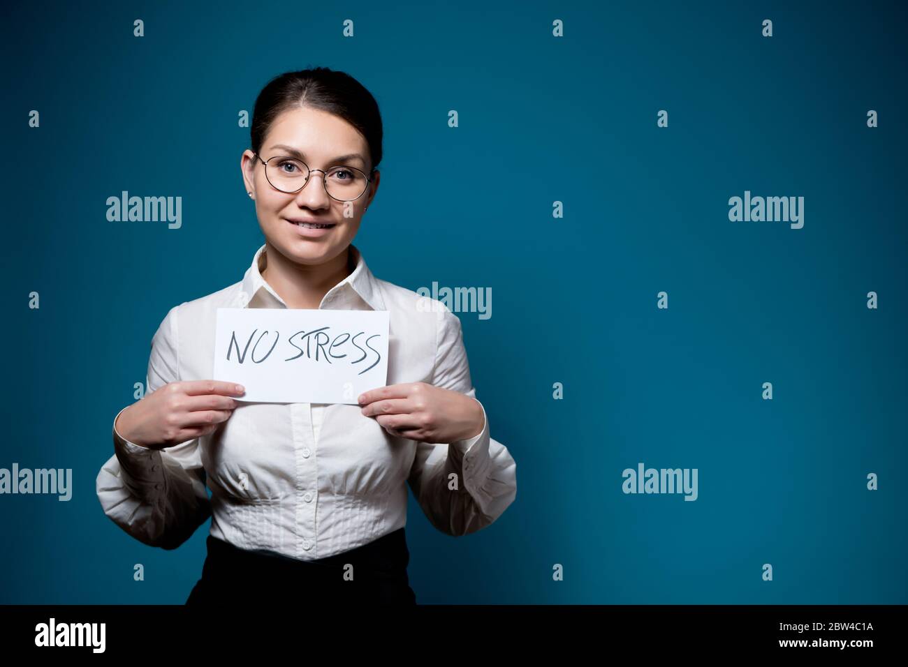 fille avec des lunettes et une chemise blanche avec un faux smile tient un morceau de papier avec les mots non stress Banque D'Images