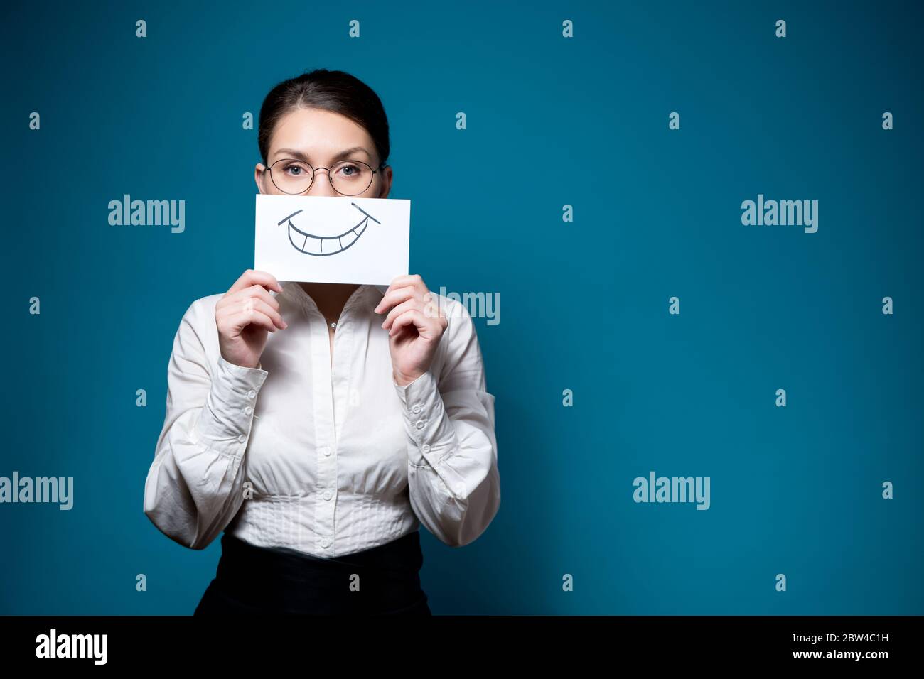 un travailleur non émotionnel couvre la moitié de son visage avec une feuille de un sourire peint Banque D'Images