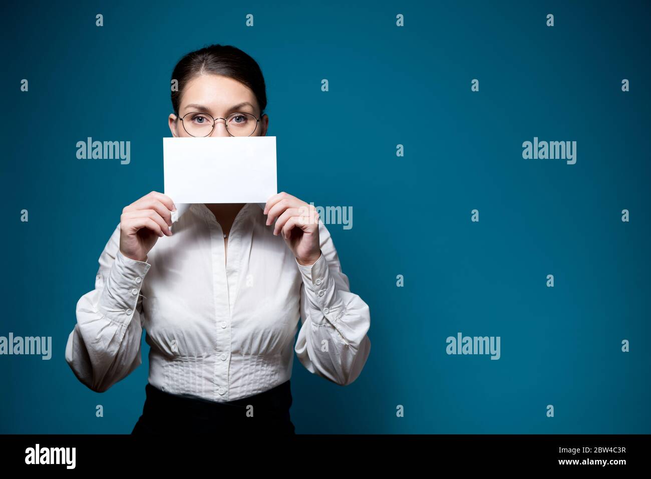 femme en chemise blanche et lunettes couvre sa bouche avec une feuille de papier vierge Banque D'Images