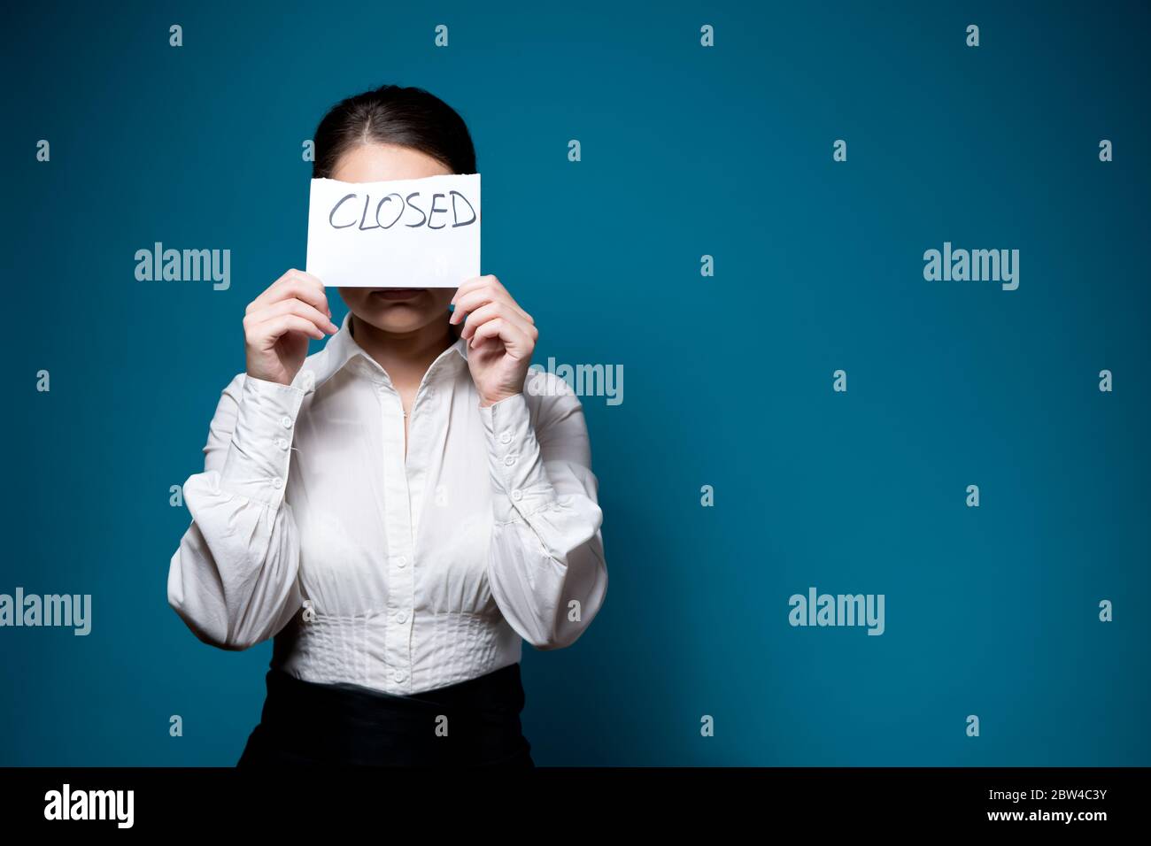 une jeune femme en chemise blanche et des lunettes couvre son visage avec un morceau de papier avec l'inscription fermée Banque D'Images