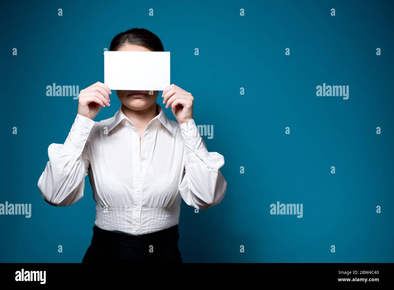 femme en chemise blanche et lunettes couvre son visage avec une feuille de papier vierge Banque D'Images