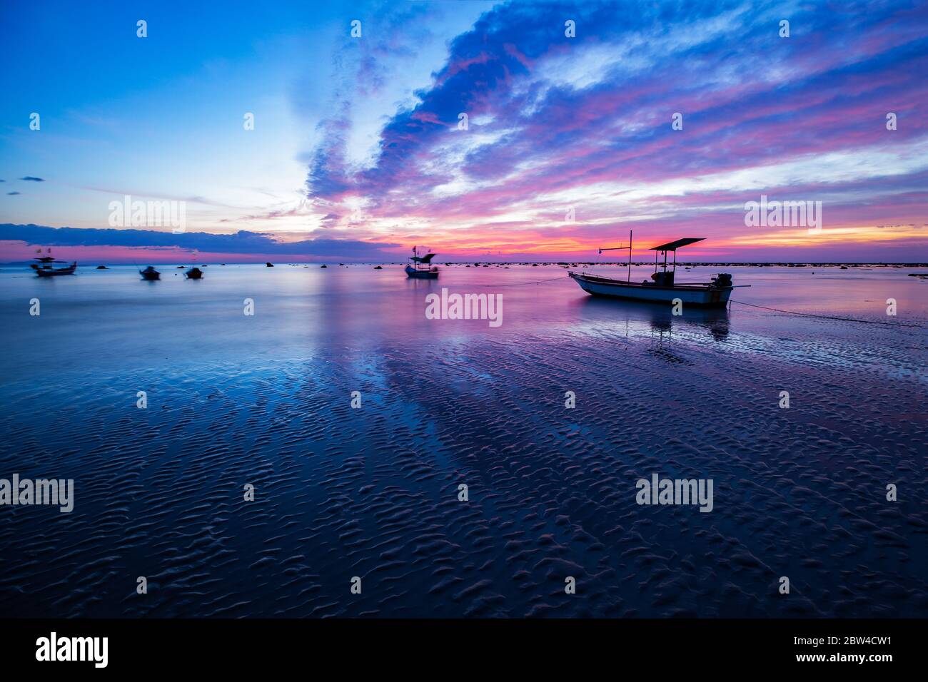 Paysage ciel coloré et bateaux de pêche amarrés tandis que la marée descend le soir à la plage de Pakarang, Takuapa, Phang Nga, Thaïlande Banque D'Images