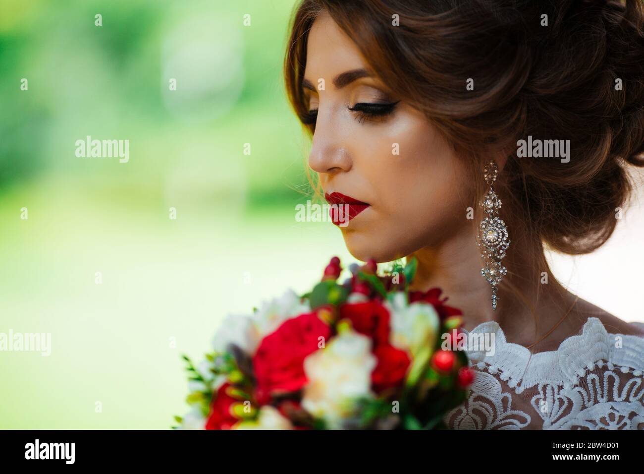 brunette mariée dans une robe avec un bouquet de mariage dans le parc sur un fond de verdure. Banque D'Images