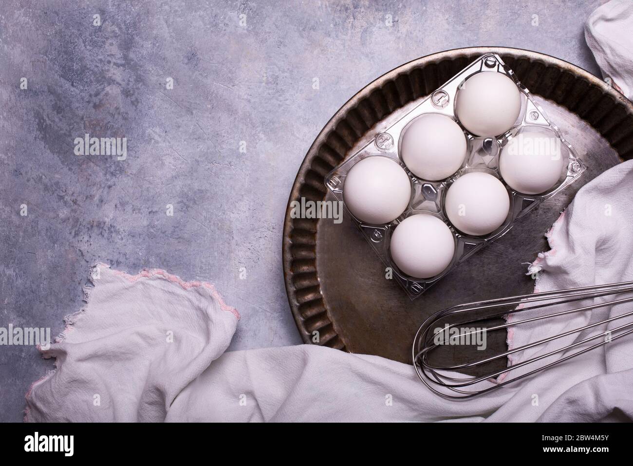 sur fond texturé gris, avec vue de dessus, une serviette de thé en coton et une demi-douzaine d'œufs blancs dans le moule à gâteau en métal pour la préparation culinaire Banque D'Images