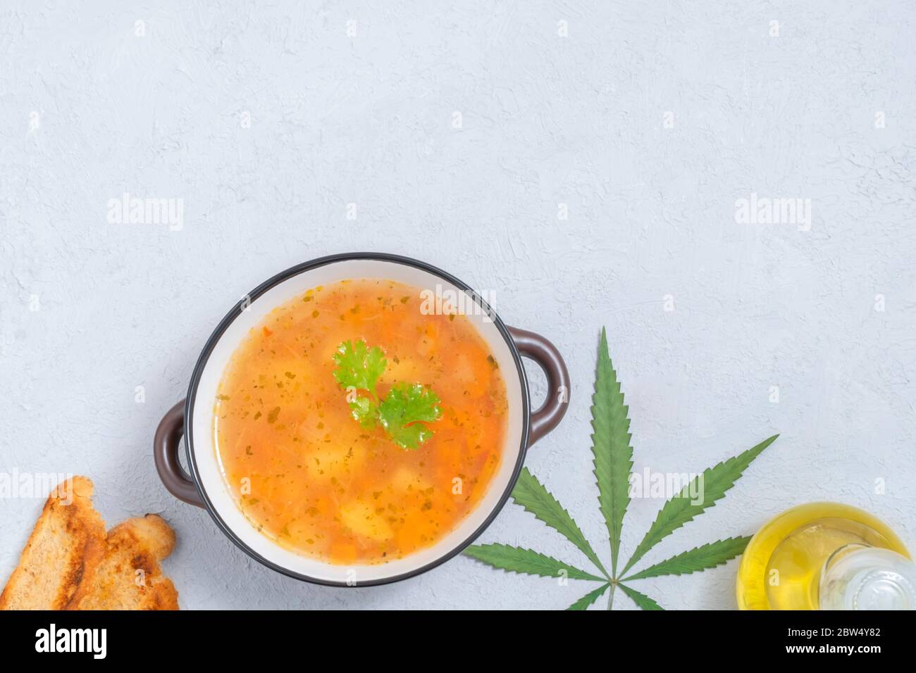 Concept alimentaire infusé au cannabis. Vue de dessus de la soupe de légumes de cannabis sur fond neutre avec feuille de marijuana, huile de cannabis, tranches de pain Banque D'Images