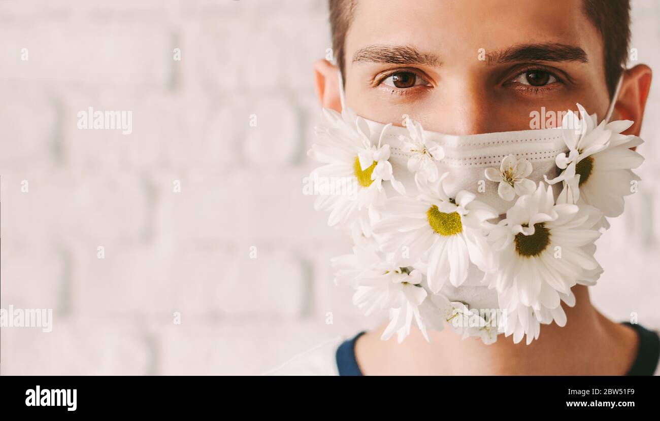 Gros plan portrait heureux homme portant un masque de protection avec fleurs de Marguerite. Jeune homme médecin en été masque médical pour la protection personnelle à nouveau Banque D'Images
